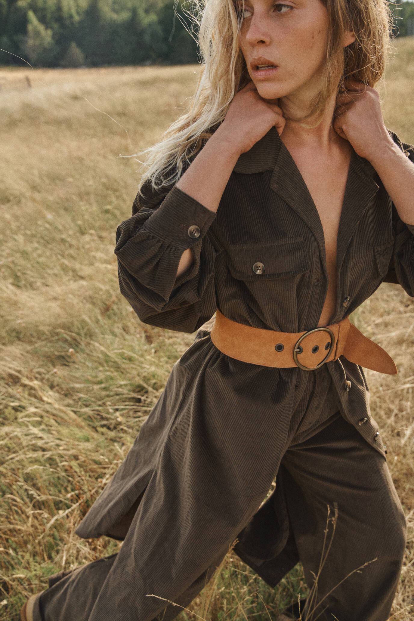 Femme portant une ceinture cognac en cuir naturel avec boucle ronde, stylisant une tenue bohème en velours côtelé dans un champ ensoleillé, qualité faite main.