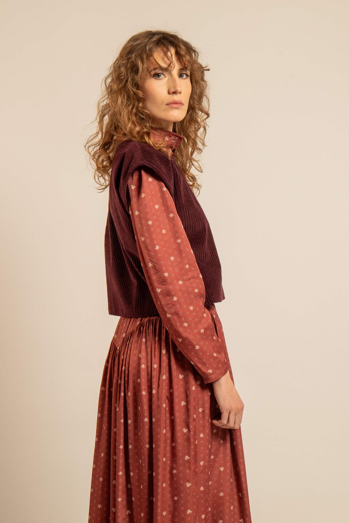 Modèle portant un top sans manches en velours côtelé bordeaux sur une blouse imprimée avec une jupe longue fleurie pour un look de superposition automne hiver 2026