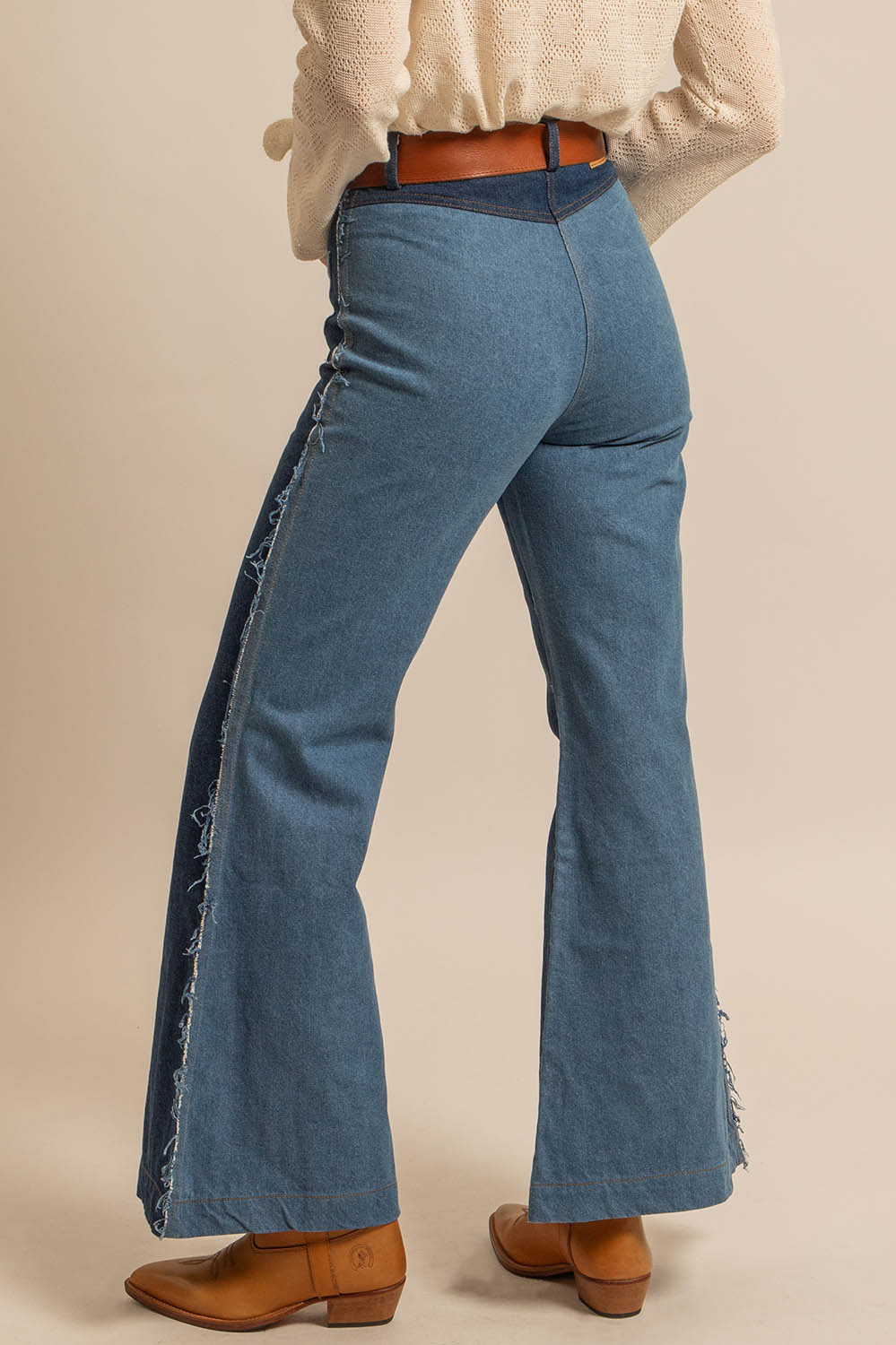 Pantalon en denim bicolore bleu avec effet déchiré sur les côtés, coupe évasée et ceinture marron, style bohème et qualité fabrication française.