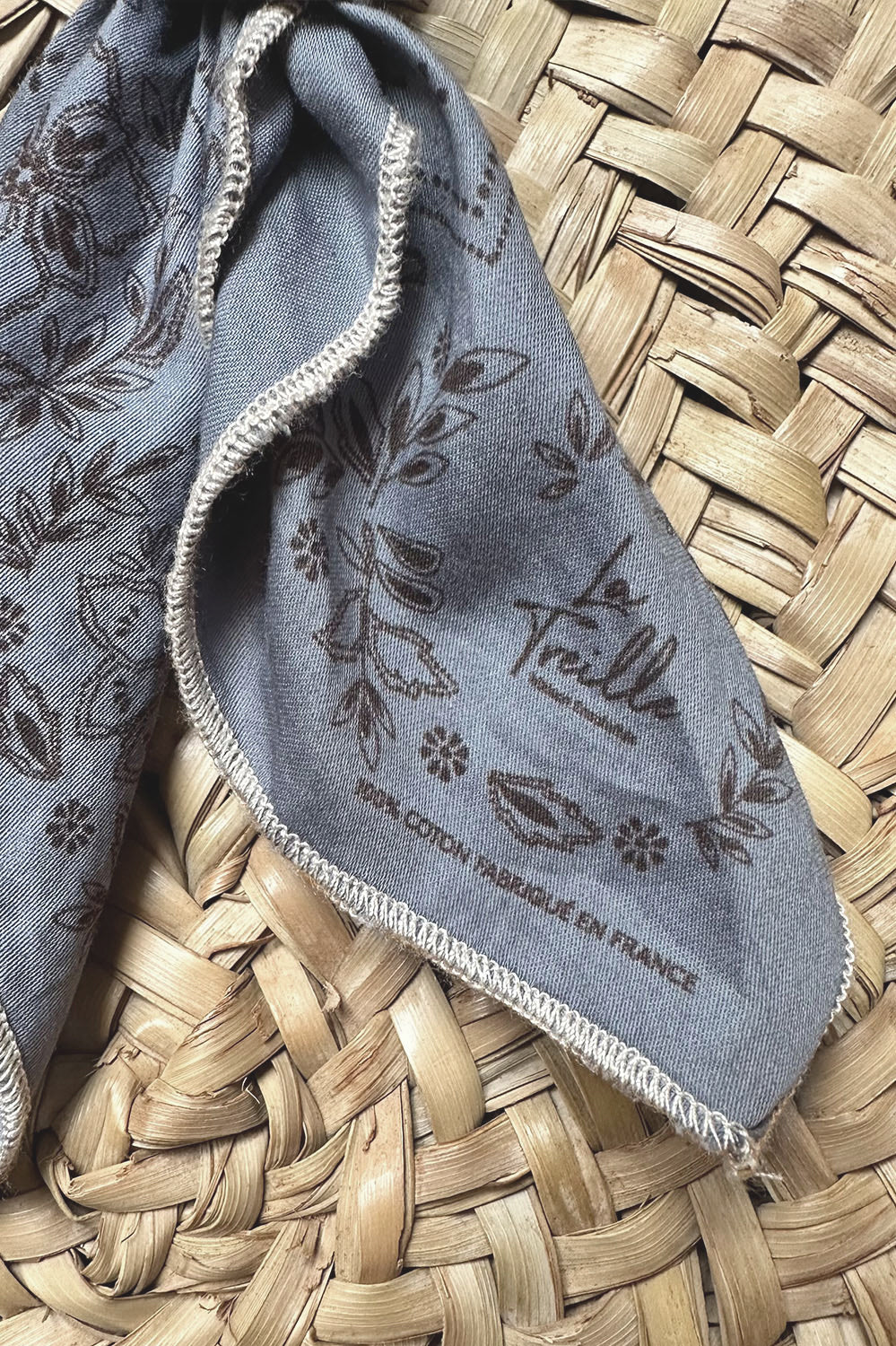 Tissu en coton bleu gris orné de motifs floraux délicats et couture beige, évoquant un style bohème et une fabrication française de qualité.