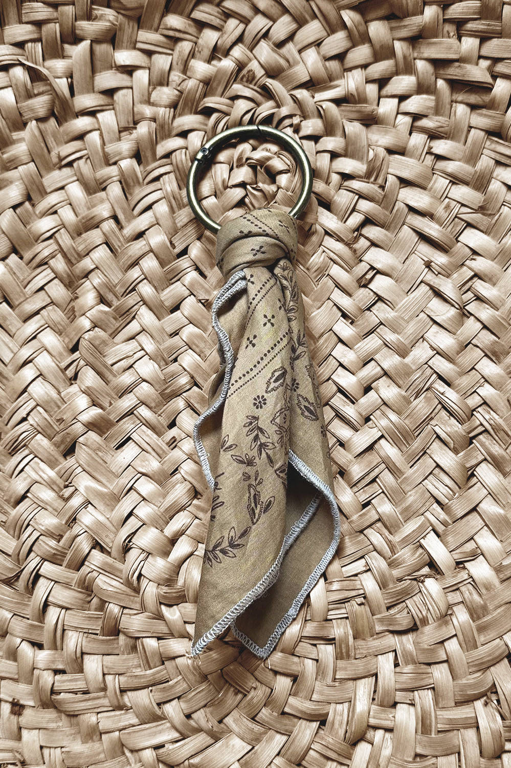 Porte-clés avec tissu en coton décoré de motifs floraux délicats, posé sur un fond en matière tressée naturelle dans un style bohème et artisanal.