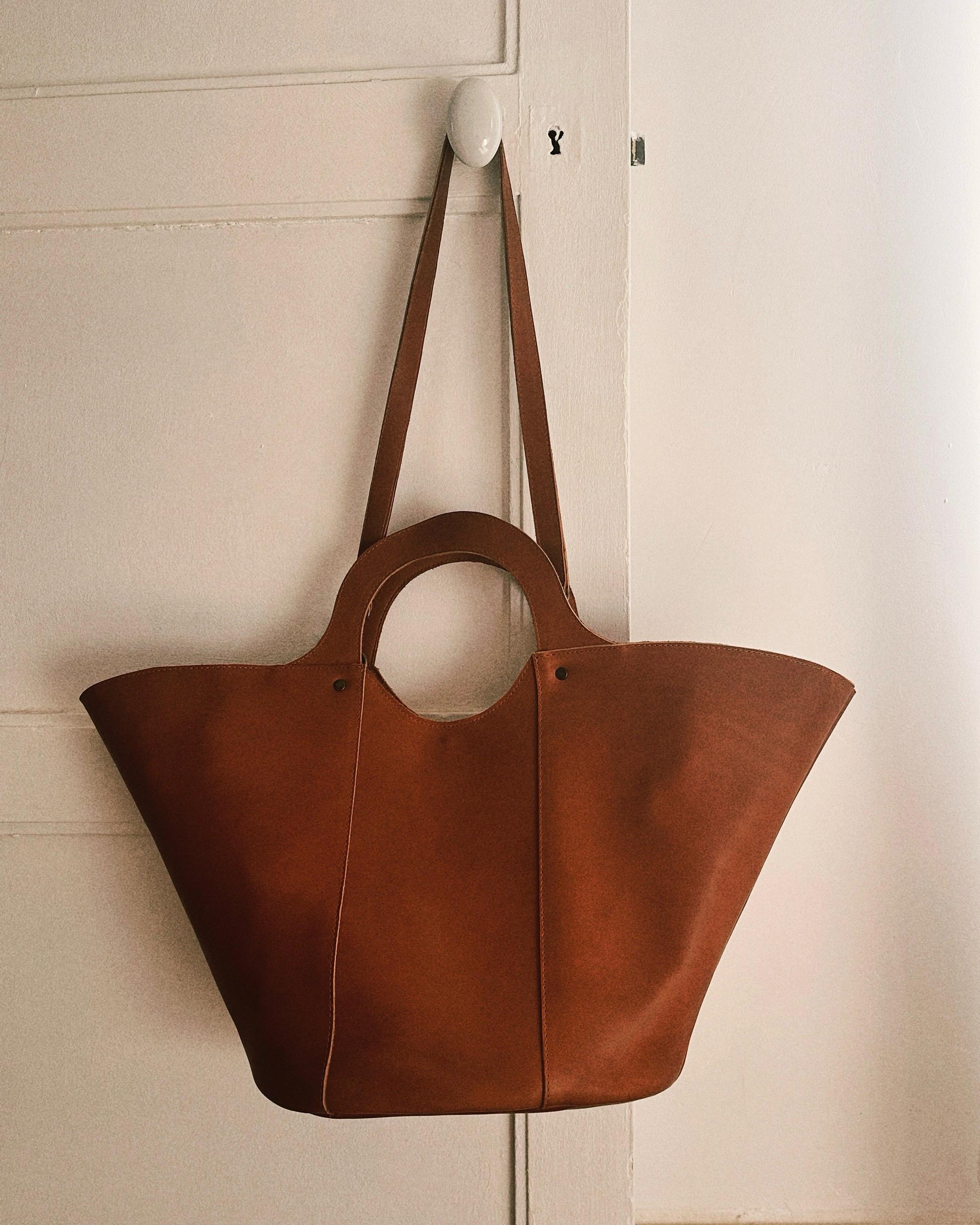 Grand cabas en cuir cognac suspendu, au design épuré avec anse longue et poignée ronde, alliant élégance et savoir-faire fait main.