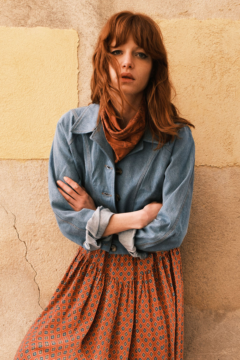 Blouson Jane en denim bleu jeans porté avec une jupe imprimée, look face contre un mur