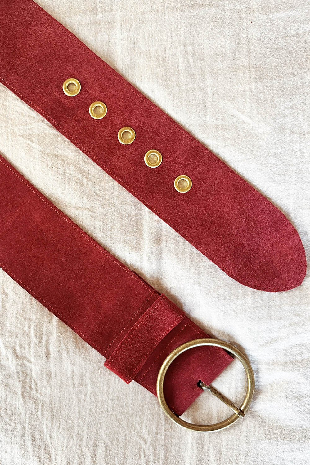 Zoom sur la boucle en laiton vieilli et les œillets dorés de la Ceinture Dolly en cuir suédé rouge sienne.