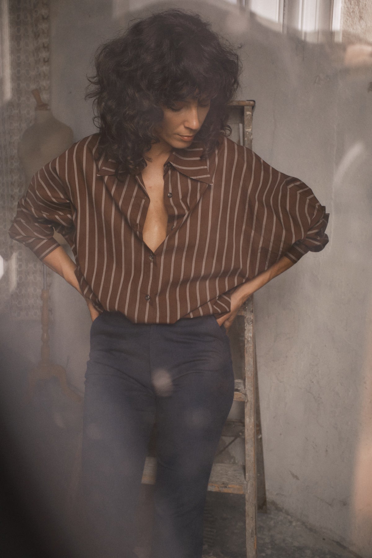 Femme portant une chemise oversize chocolat à rayures et manches chauve-souris avec un pantalon sombre dans un décor chaleureux inspiré des années 70
