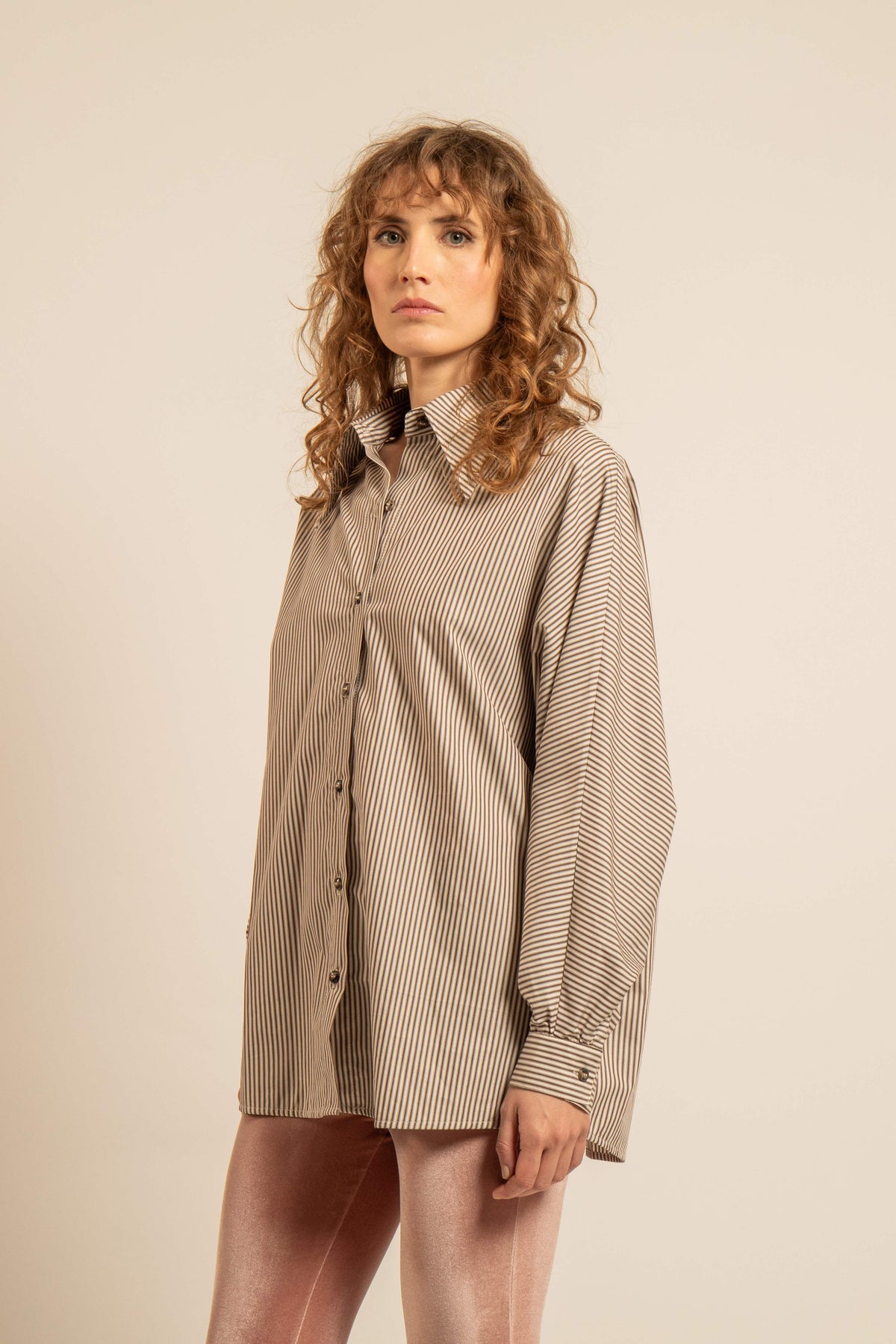 Modèle portant une chemise oversize vanille à fines rayures avec col pelle à tarte et manches chauve souris inspirée des années 70