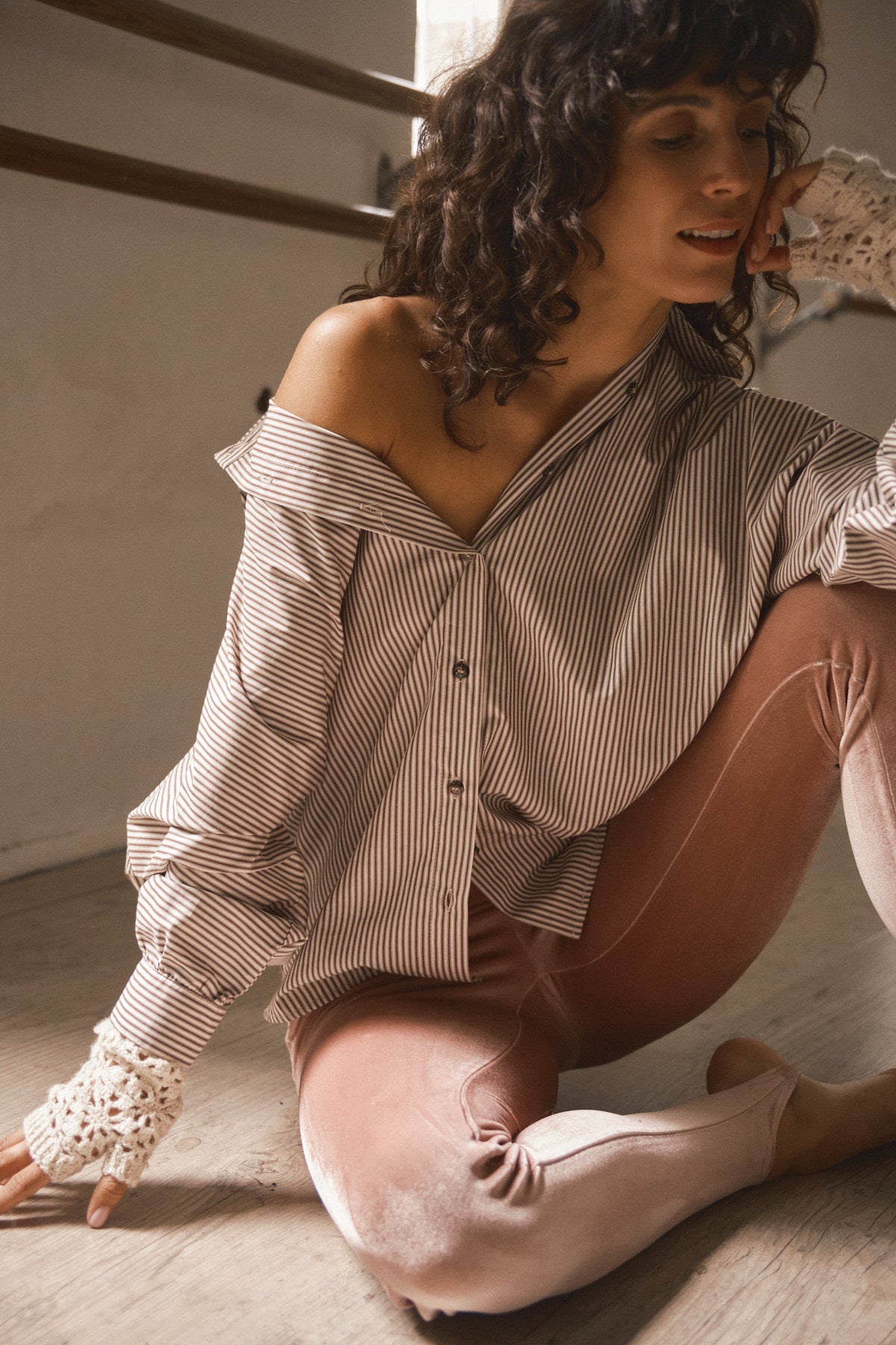 Femme portant une chemise rayée en coton à la coupe oversize avec col large et manches amples dans un intérieur lumineux esprit années 70
