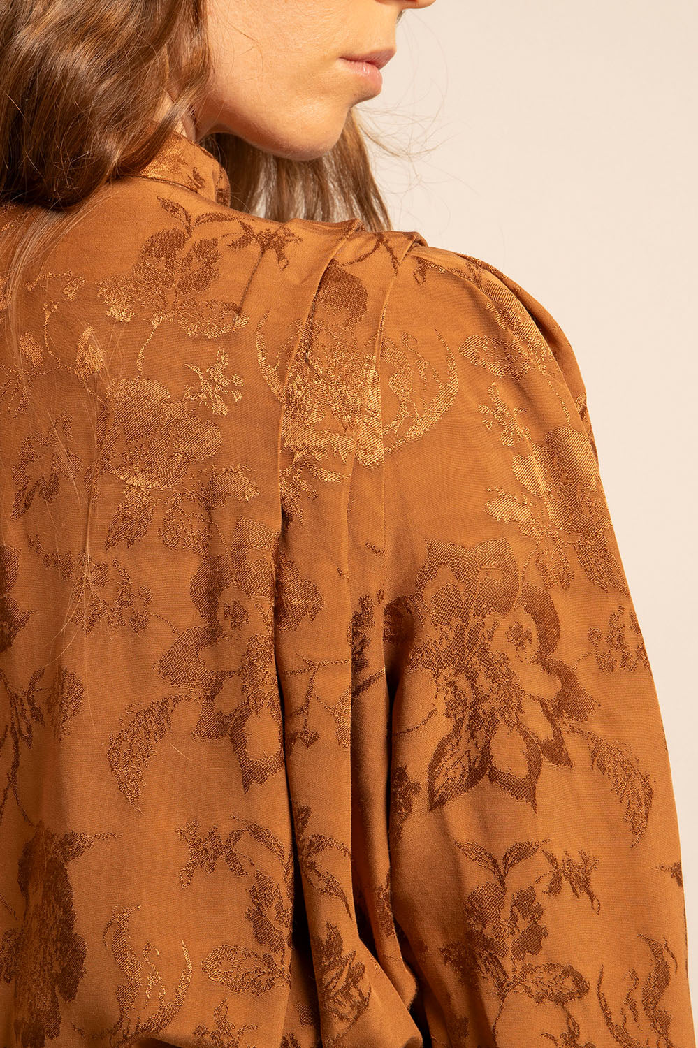 Zoom sur les détails du tissu jacquard floral et les plis de l’épaule.