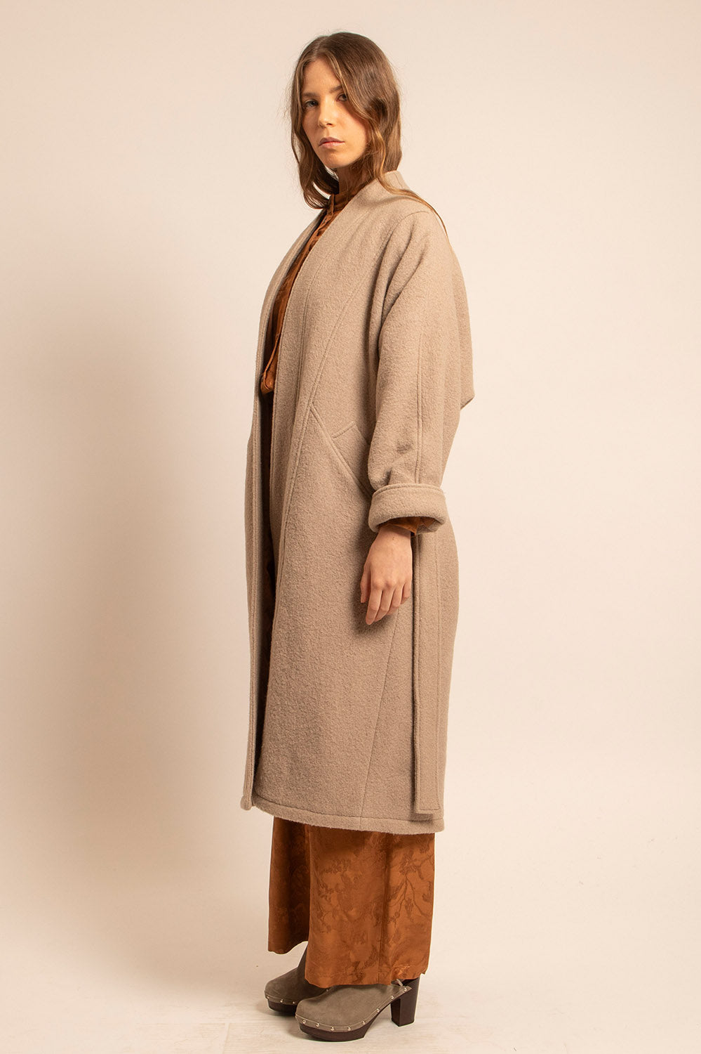 Manteau long en laine beige vu de profil, avec poches et coupe kimono