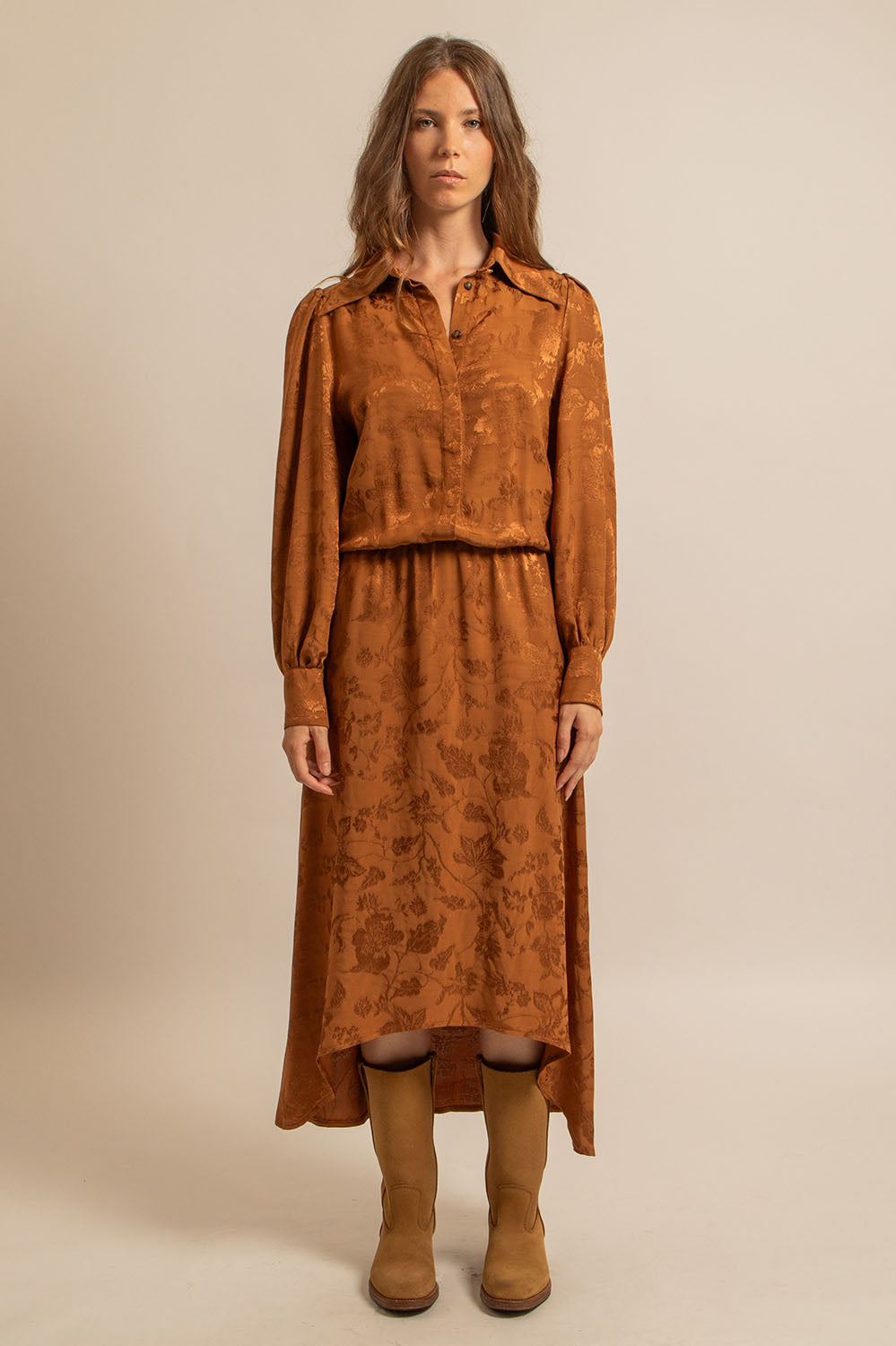 Femme portant la robe Paulette en jacquard cognac, vue de face, avec des bottes camel.