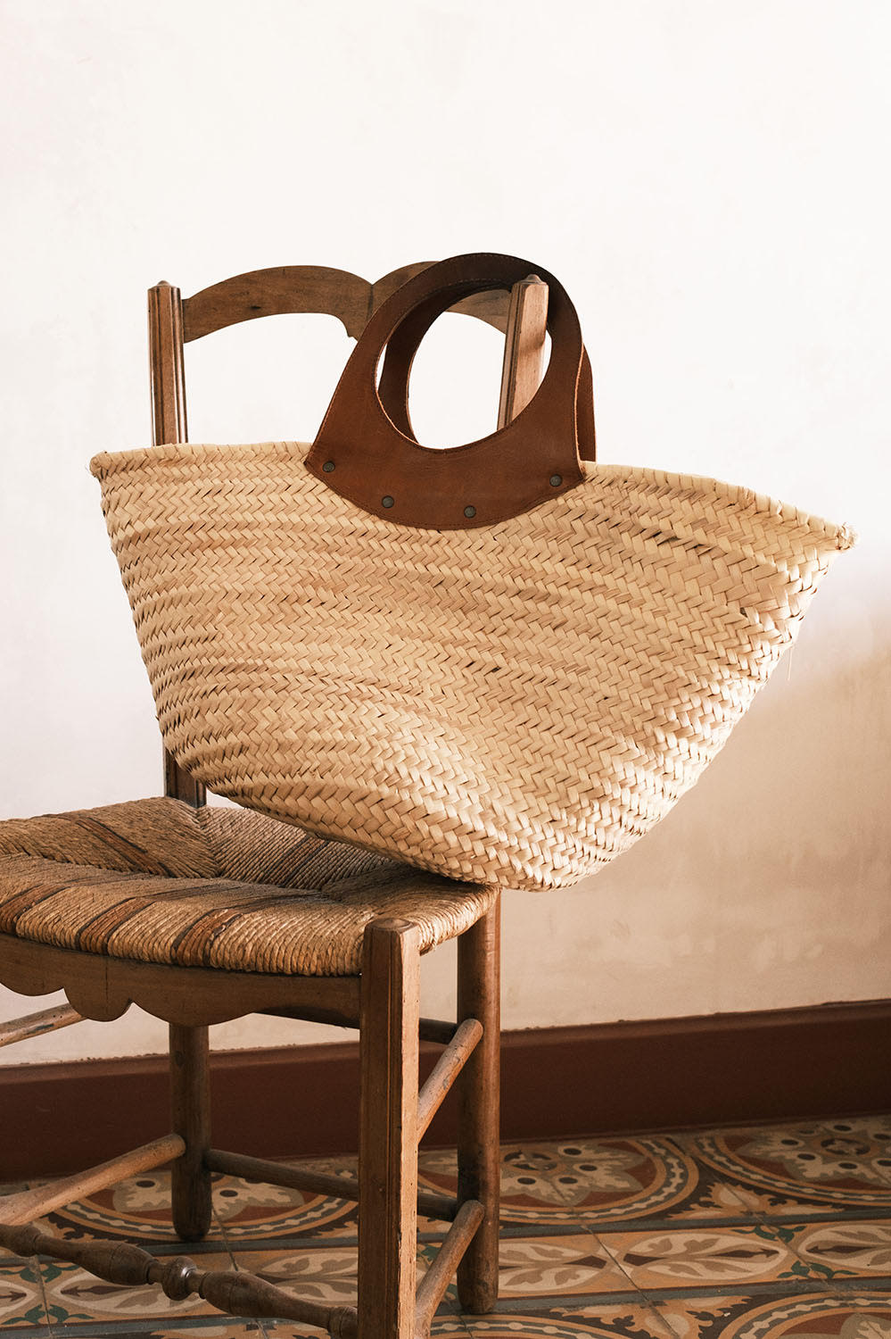 Panier en osier La Treille posé sur une chaise rustique, détail des poignées en cuir