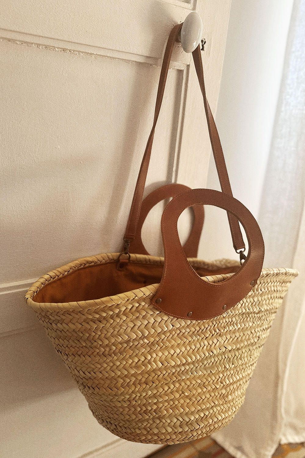 Panier en osier suspendu à un crochet mural, détail des anses en cuir marron