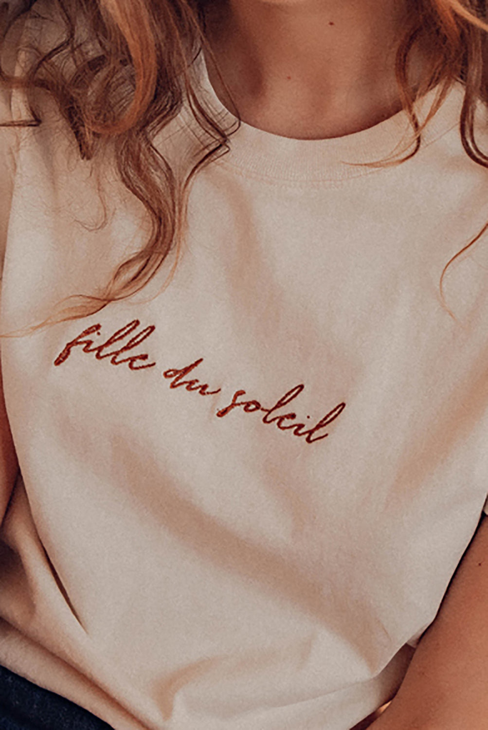 Gros plan sur la broderie "Fille du Soleil" du tee-shirt en coton bio naturel.