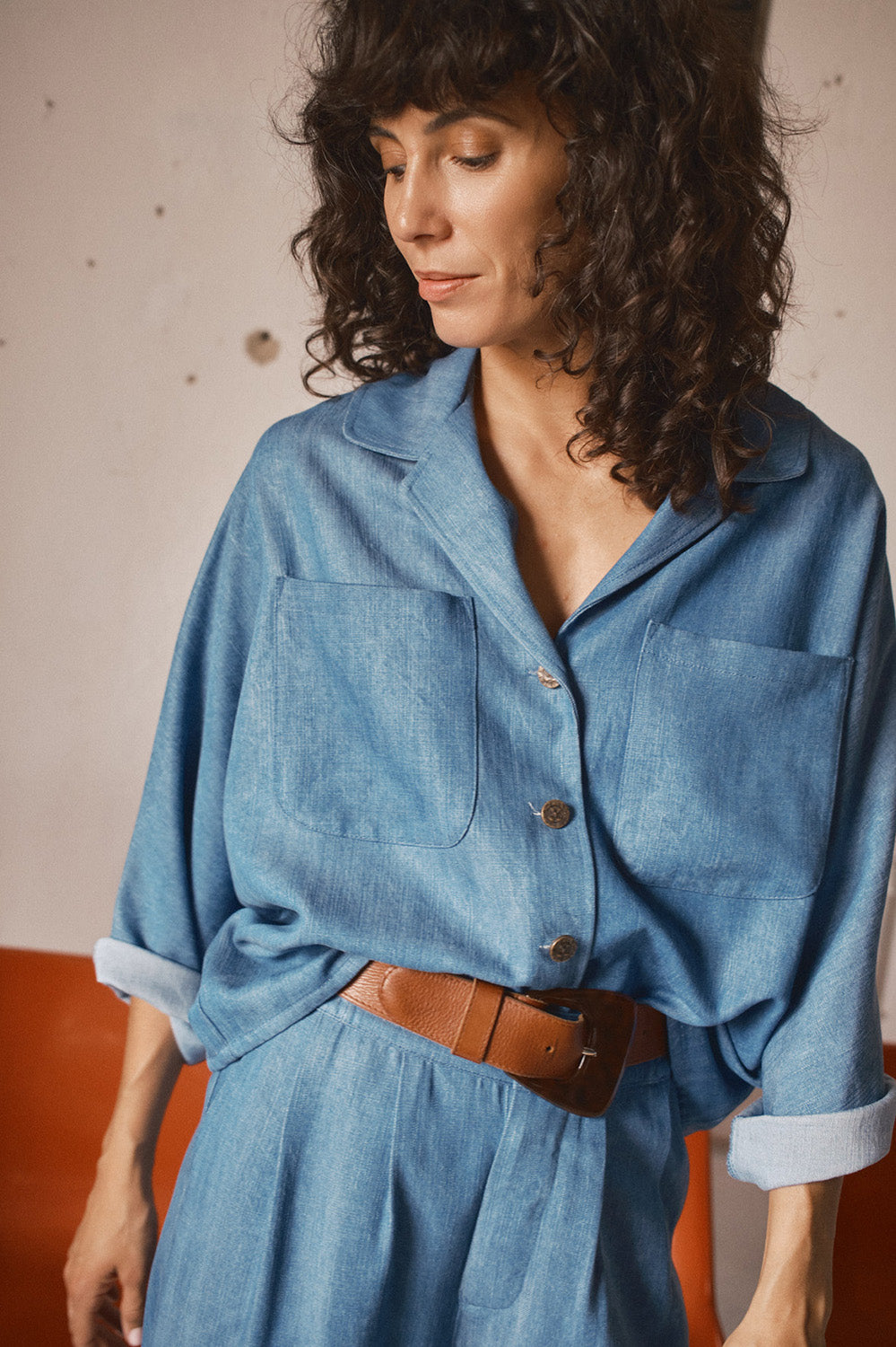 Femme portant une tenue bleue en denim avec une ceinture en cuir tabac à boucle brune esprit années 70 style élégant et décontracté