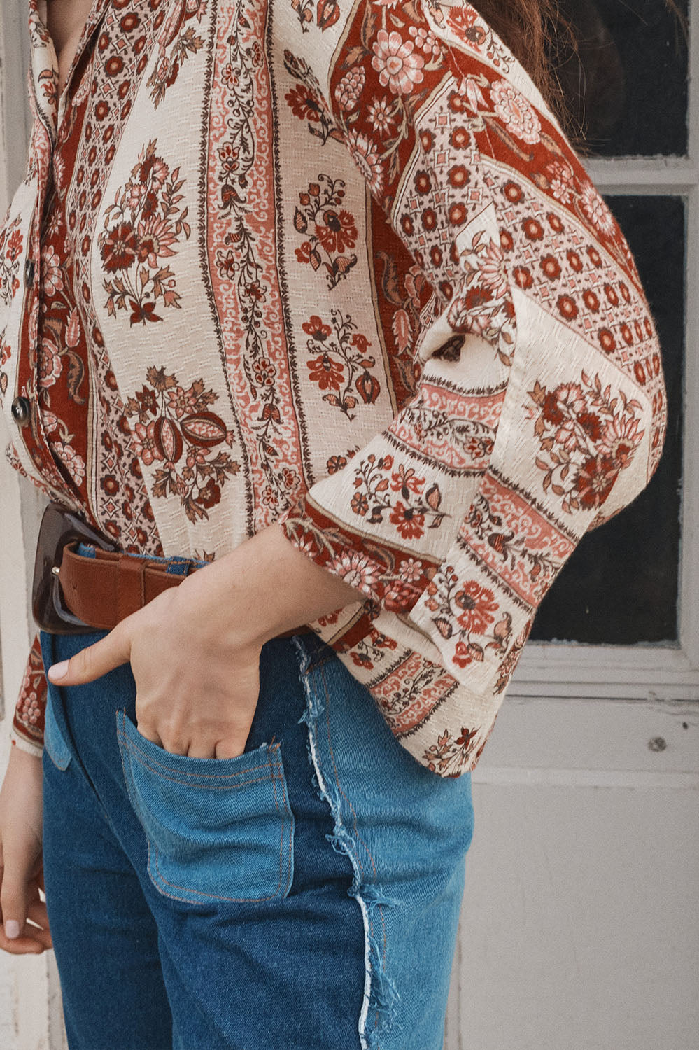 Gros plan sur un pantalon en denim bicolore bleu avec une poche apparente, porté avec une chemise à motifs floraux dans des tons beige et rouille, style bohème.