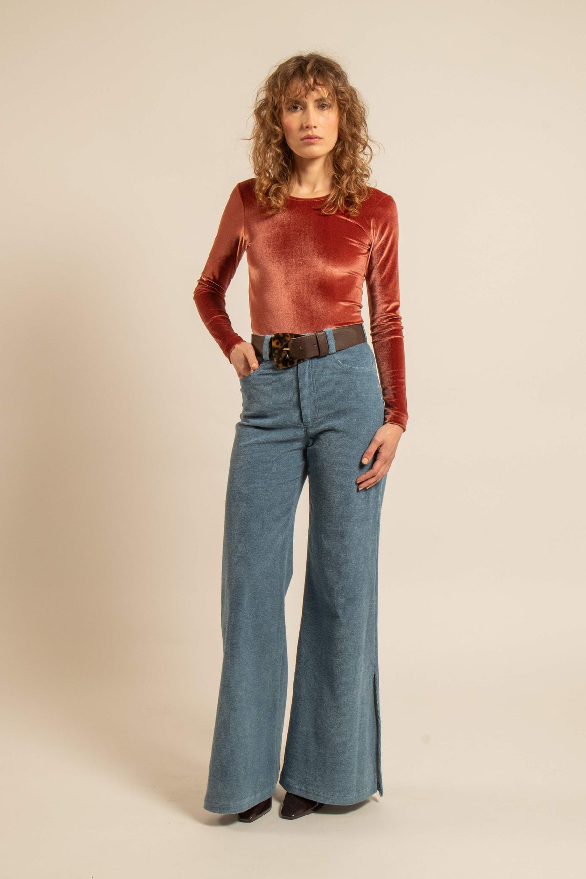 Modèle portant un body en velours ras couleur blush à manches longues avec un pantalon en jean taille haute dans un style féminin et dansant
