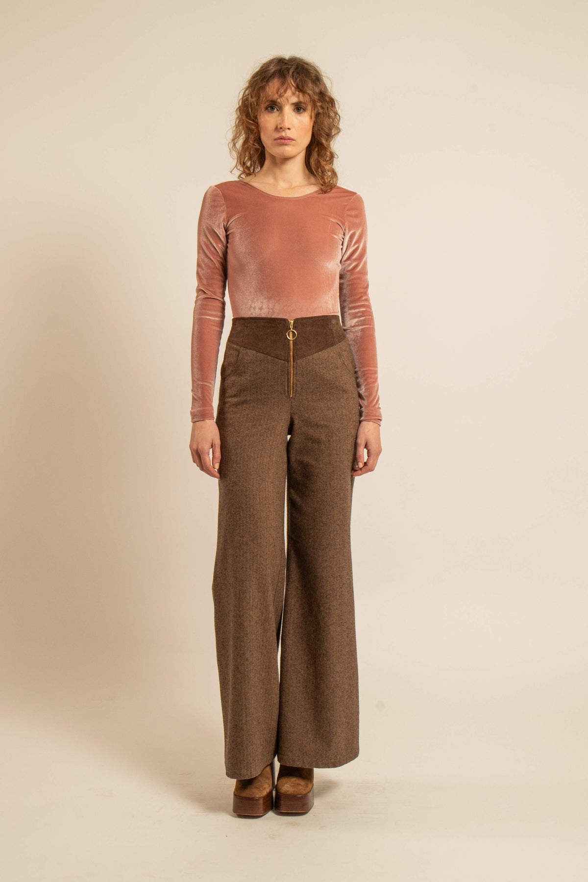 Modèle portant un body en velours rose terracotta à manches longues avec un pantalon brun à jambes larges et des escarpins assortis