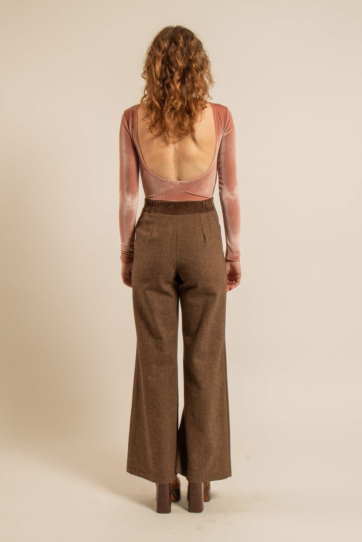 Vue de dos d’un pantalon marron taille haute à jambes évasées, porté avec un body rose, issu de la collection Automne-Hiver 2026