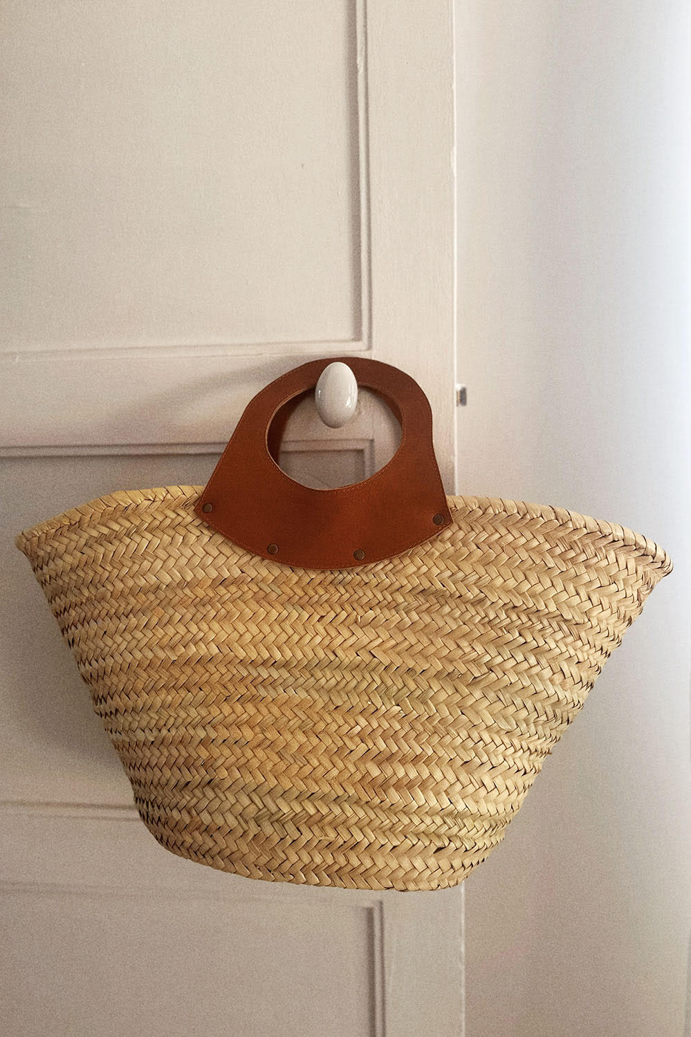 Panier en osier suspendu à un crochet mural, détail des anses en cuir marron