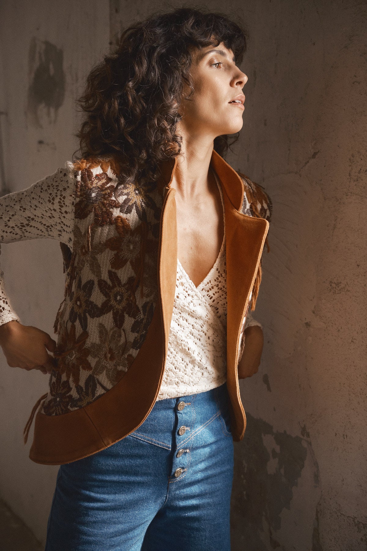 Femme portant un pantalon en denim bleu taille haute avec boutons sur le devant accompagné d un top écru crocheté et d une veste marron vintage