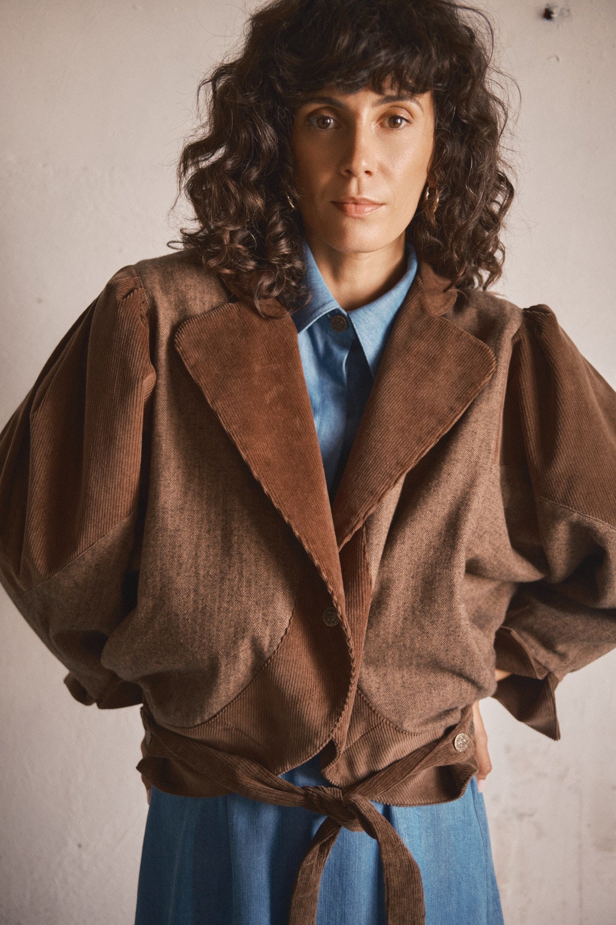Femme portant une veste marron oversize à col tailleur et ceinture nouée, superposée à une chemise bleue pour une silhouette décontractée.